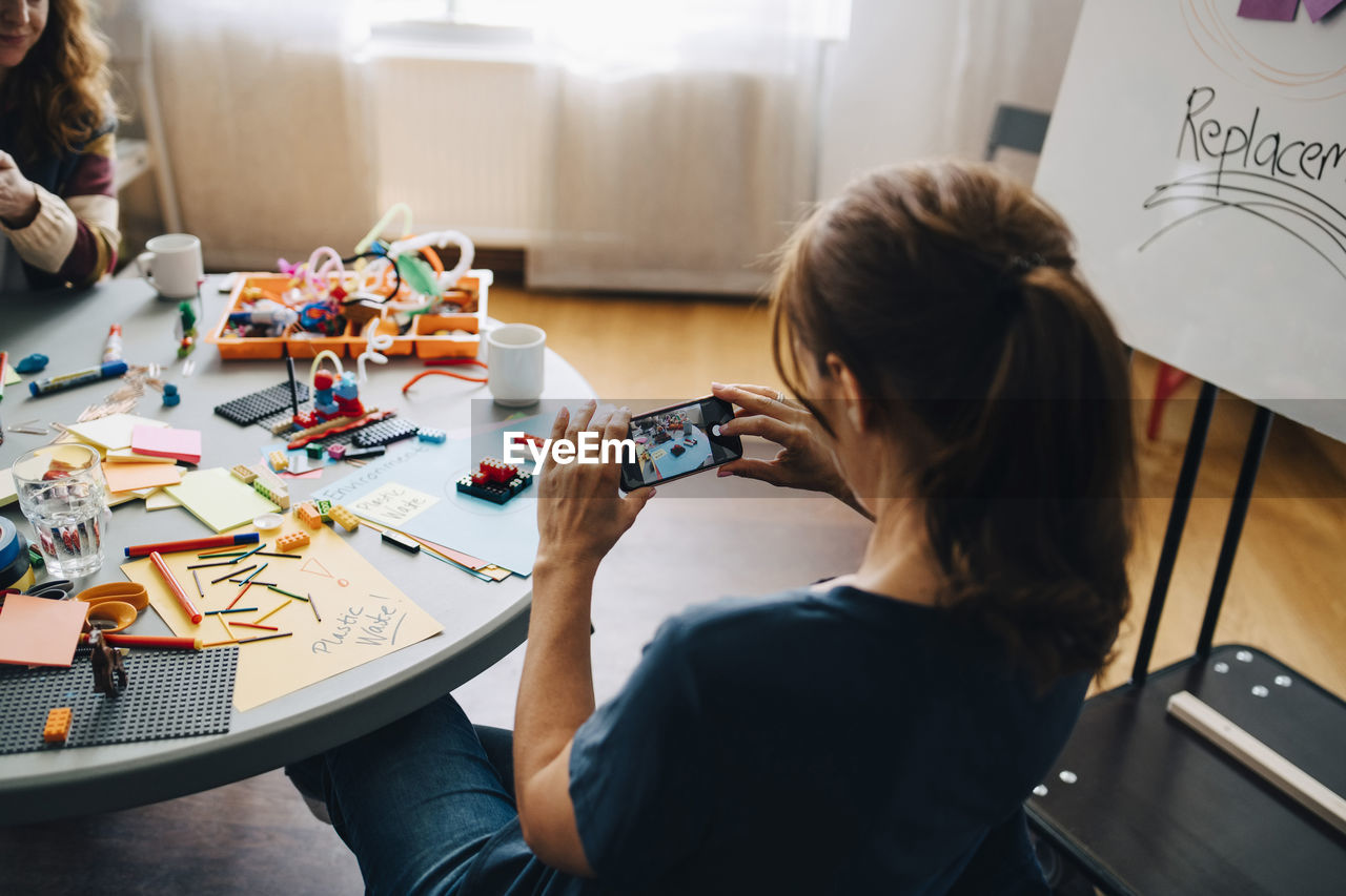 High angle rear view of businesswoman photographing stationery on table at creative office