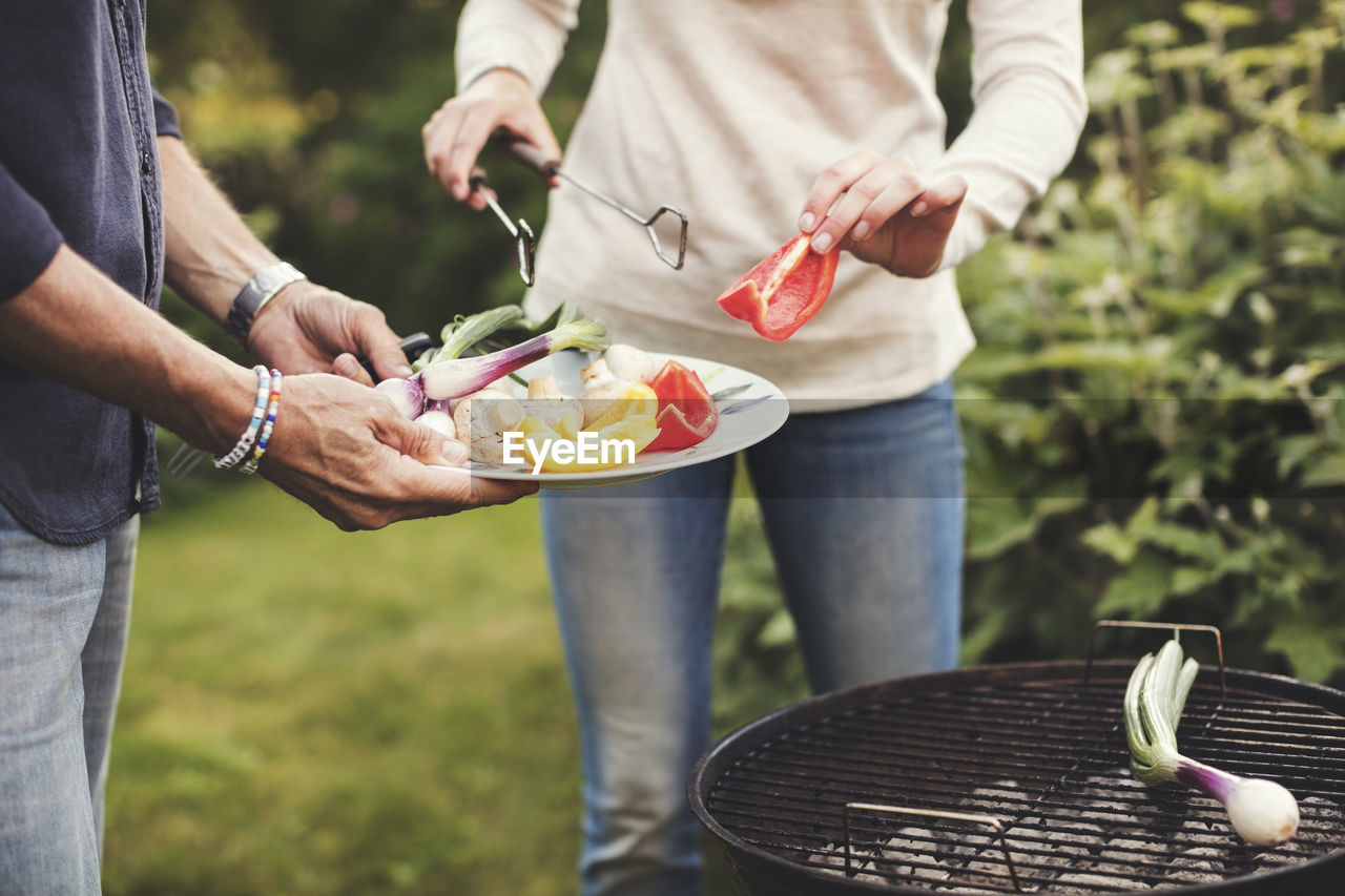 Midsection of father and daughter cooking vegetables on barbecue grill in back yard