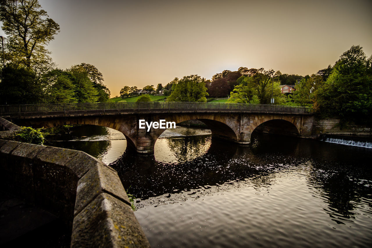 BRIDGE OVER RIVER BY TREES AGAINST SKY