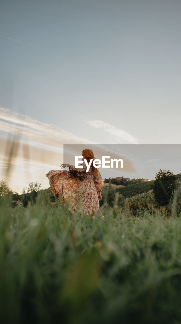 Redhead woman in a grassy field against sky