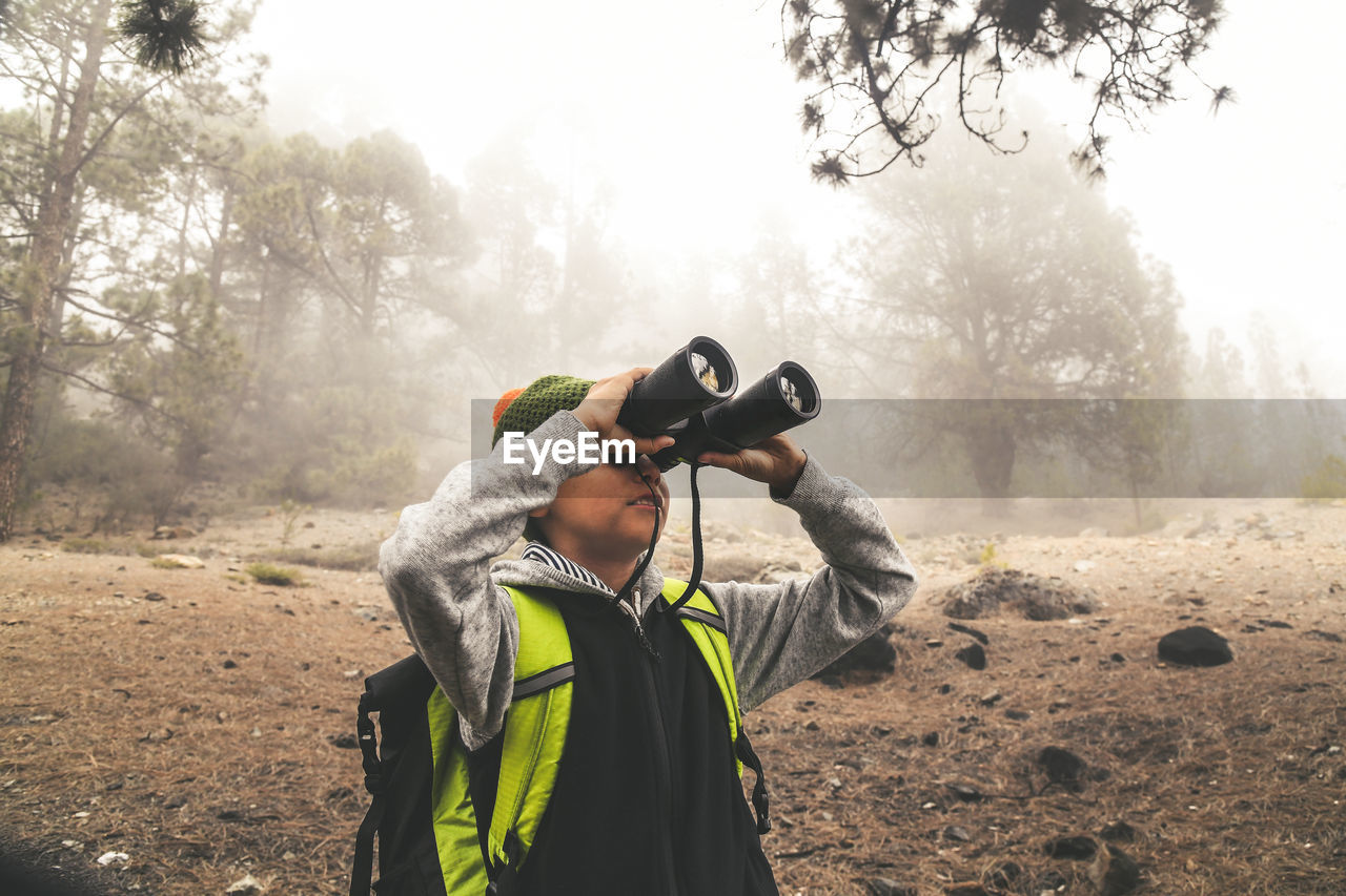 Boy looking through binoculars at forest