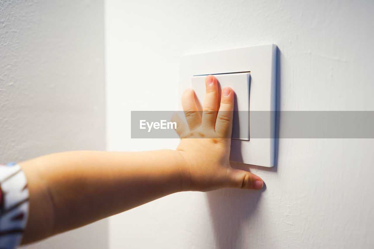 Cropped hand of child pressing light switch at home