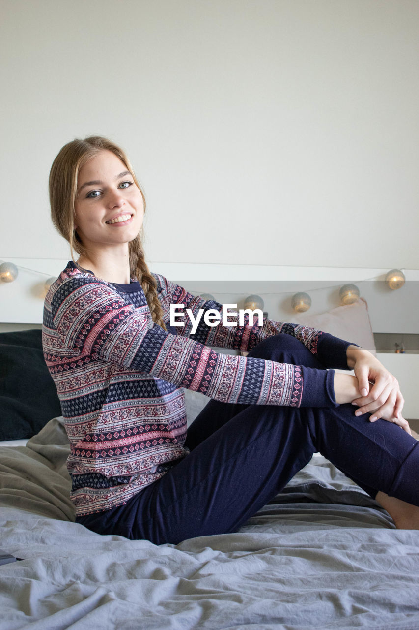 PORTRAIT OF YOUNG WOMAN SITTING ON BED