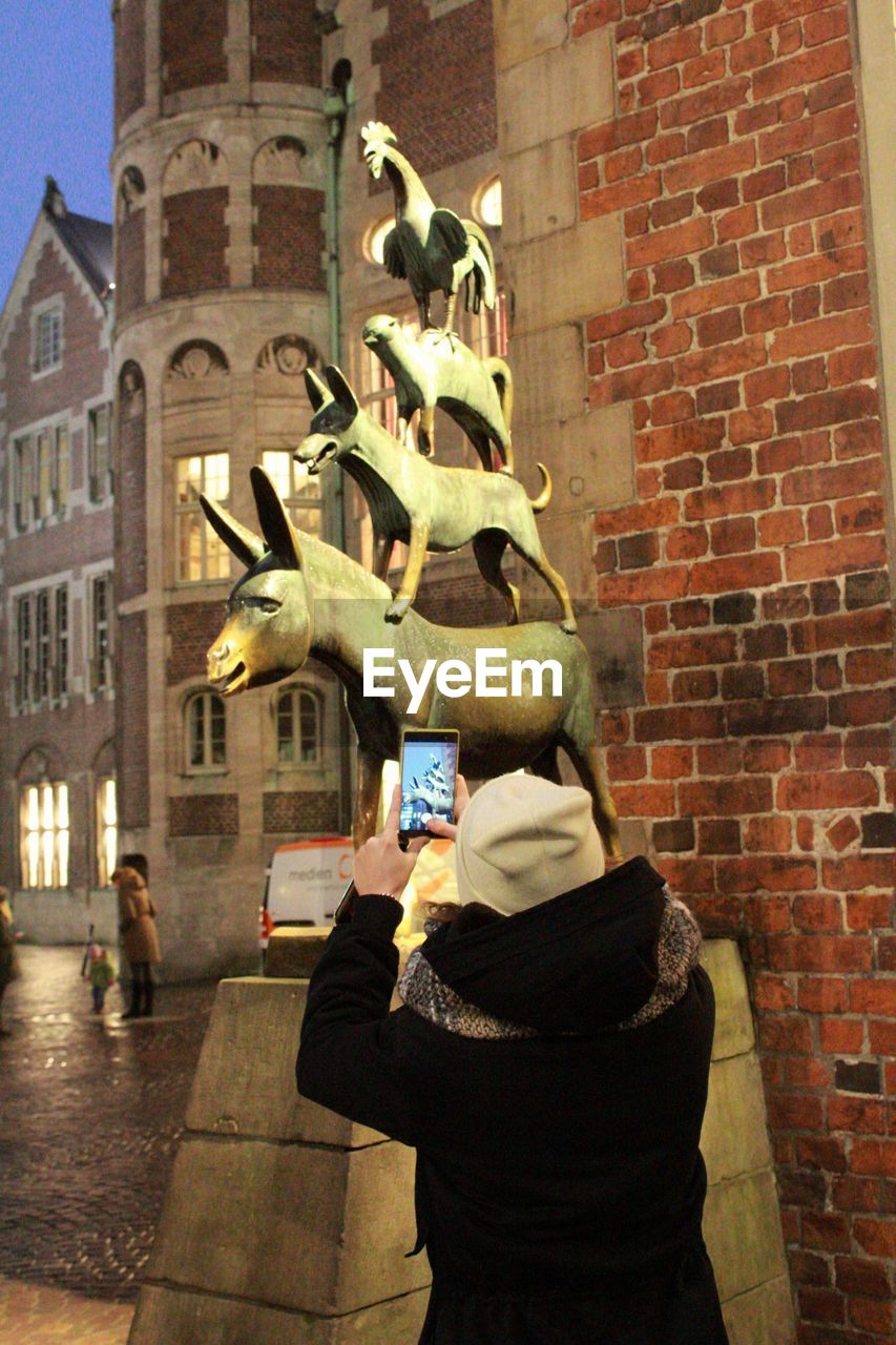 MAN PHOTOGRAPHING STATUE IN CITY