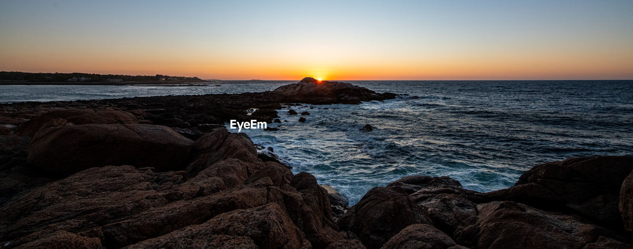 SCENIC VIEW OF ROCKS ON SEA AGAINST SKY DURING SUNSET