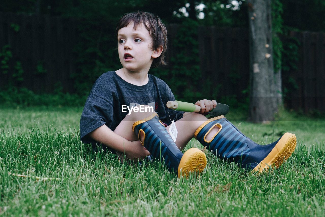 Full length of boy looking away while sitting on grassy field