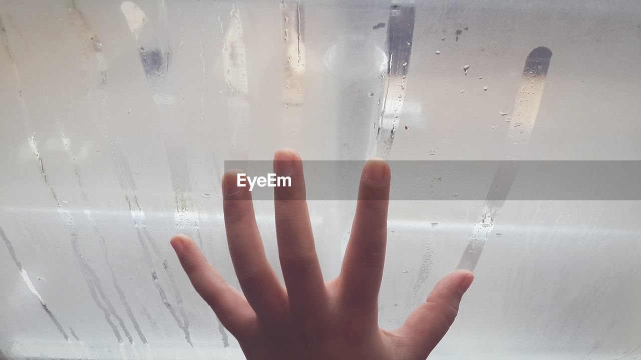 Cropped hand on condensed window in bathroom