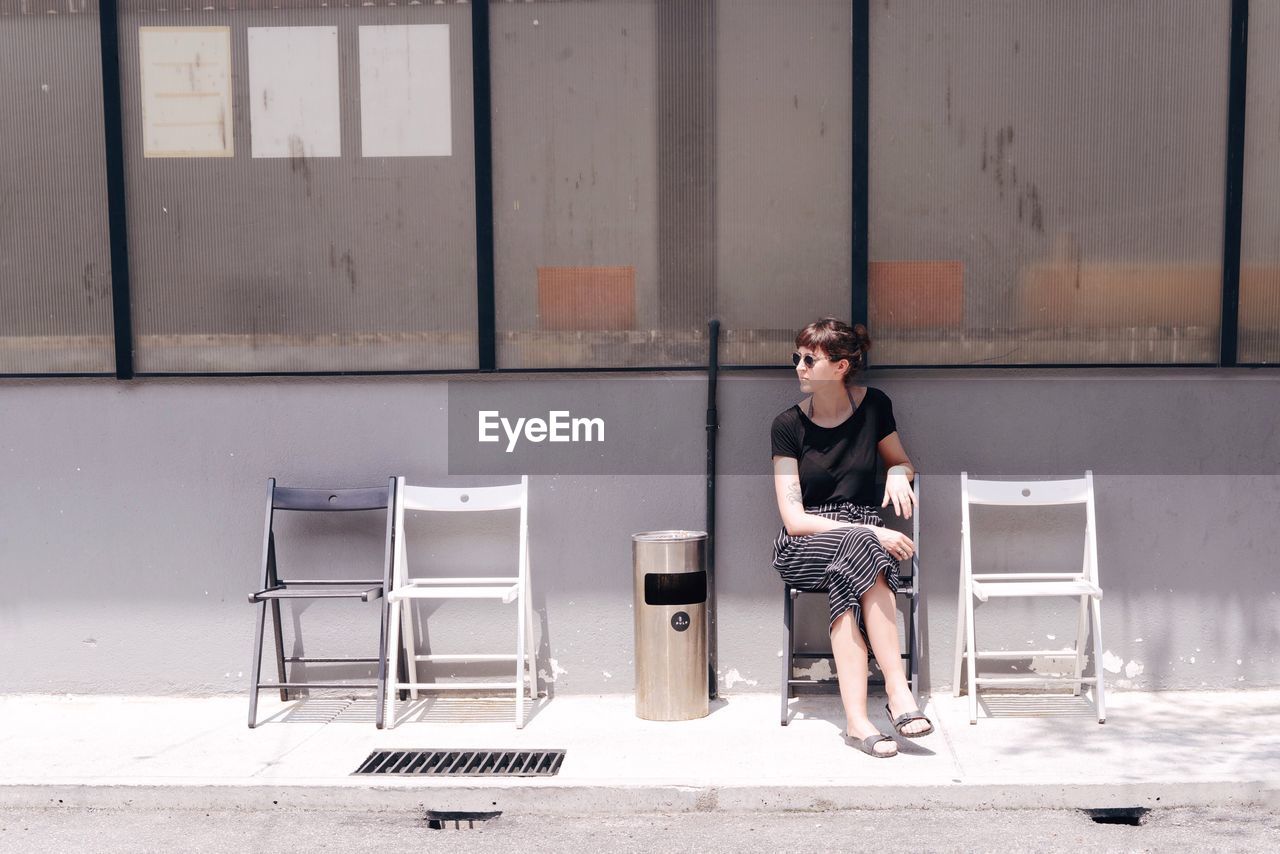 Young woman sitting on chair at sidewalk