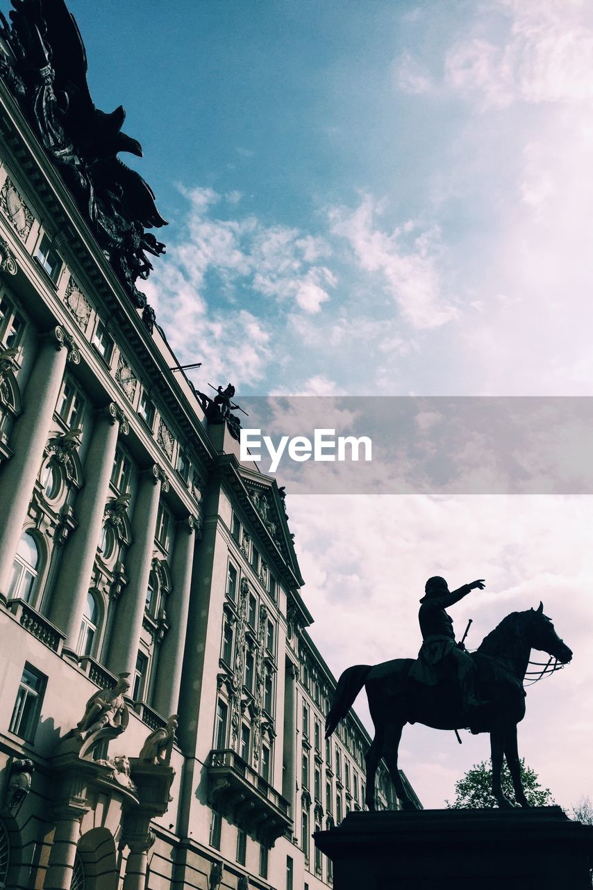 Low angle view of statue by historic building against sky