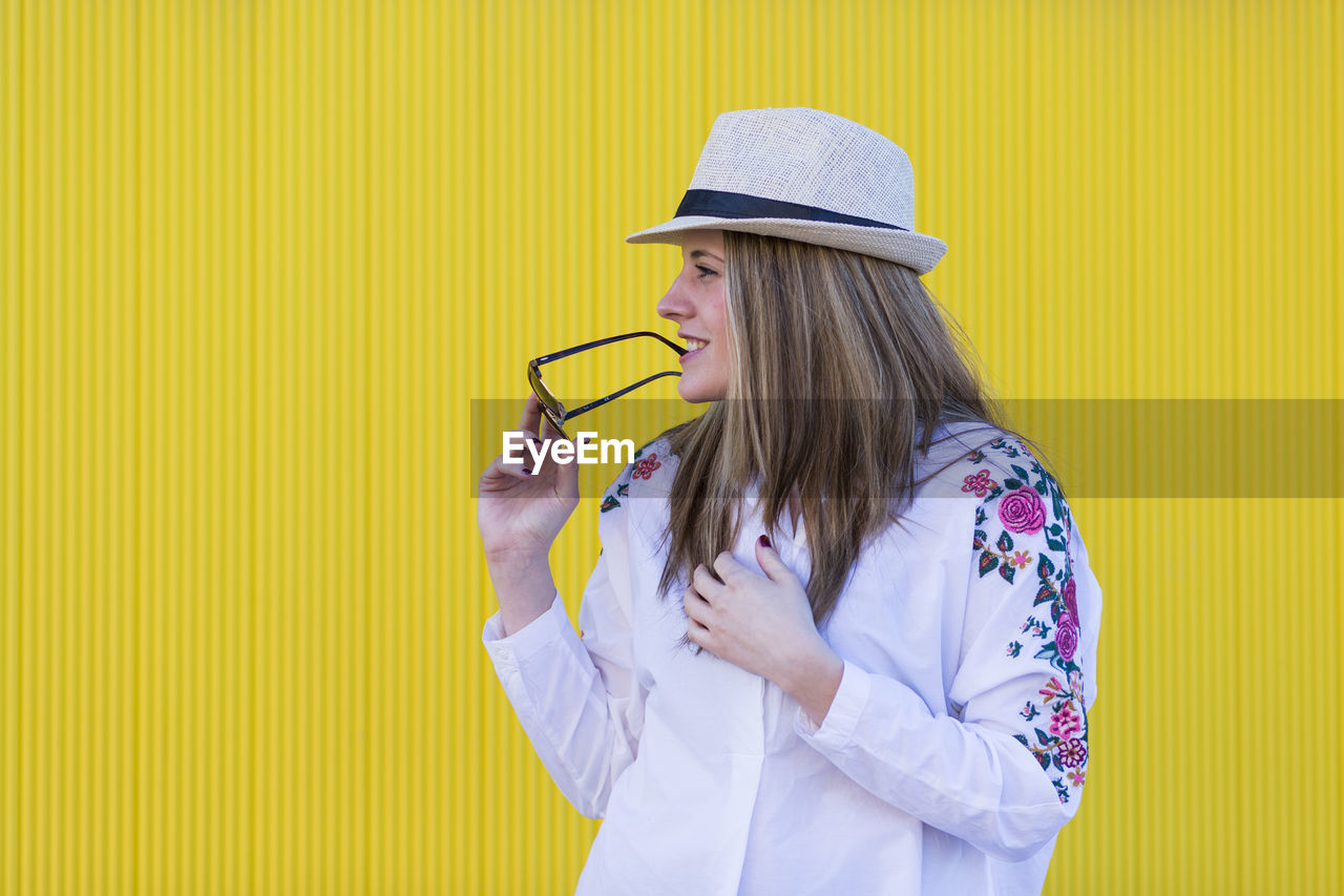 Woman looking away while standing against yellow wall