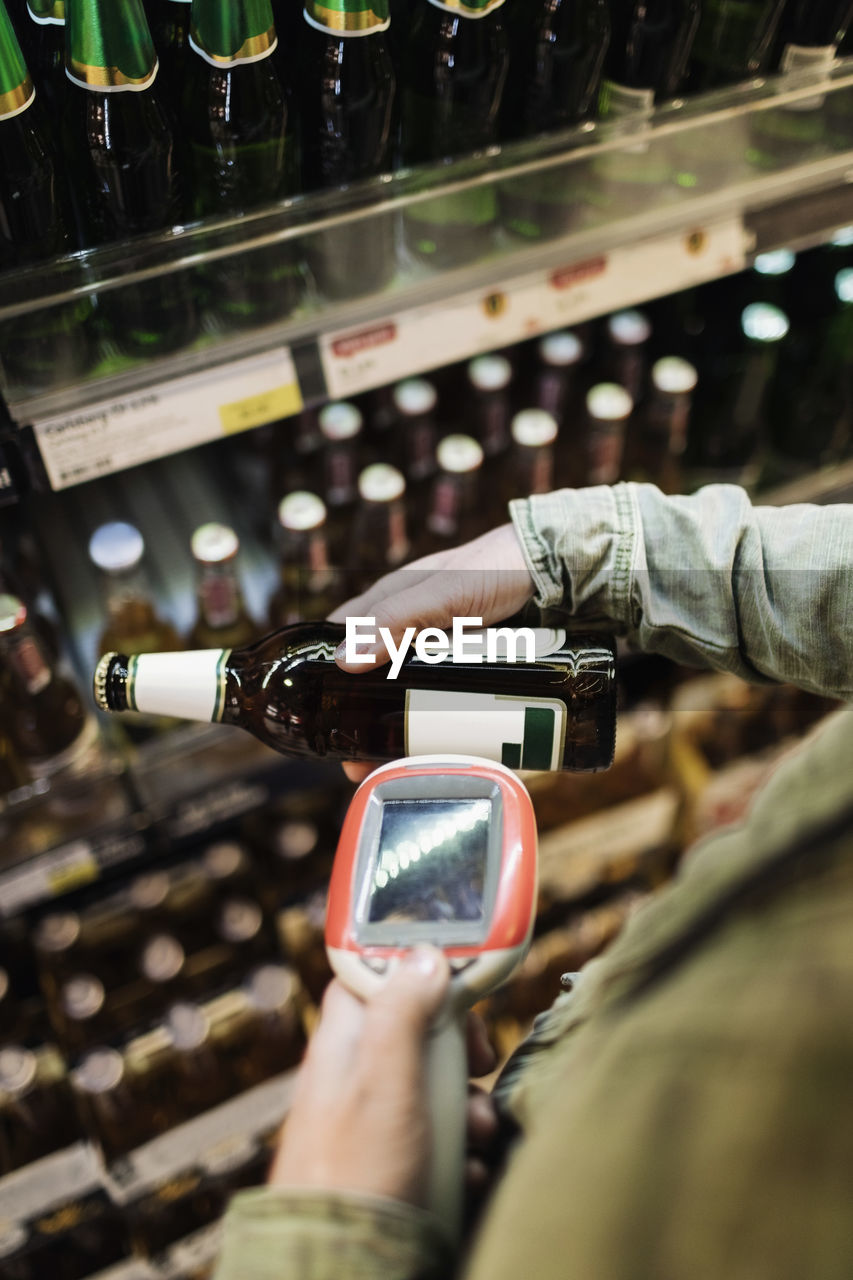 Cropped image of female customer scanning beer bottle in supermarket