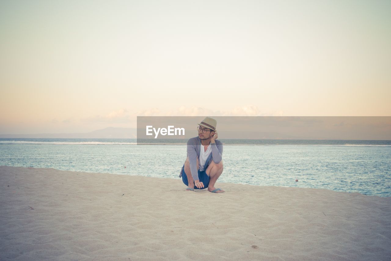 Young man crouching at sandy beach