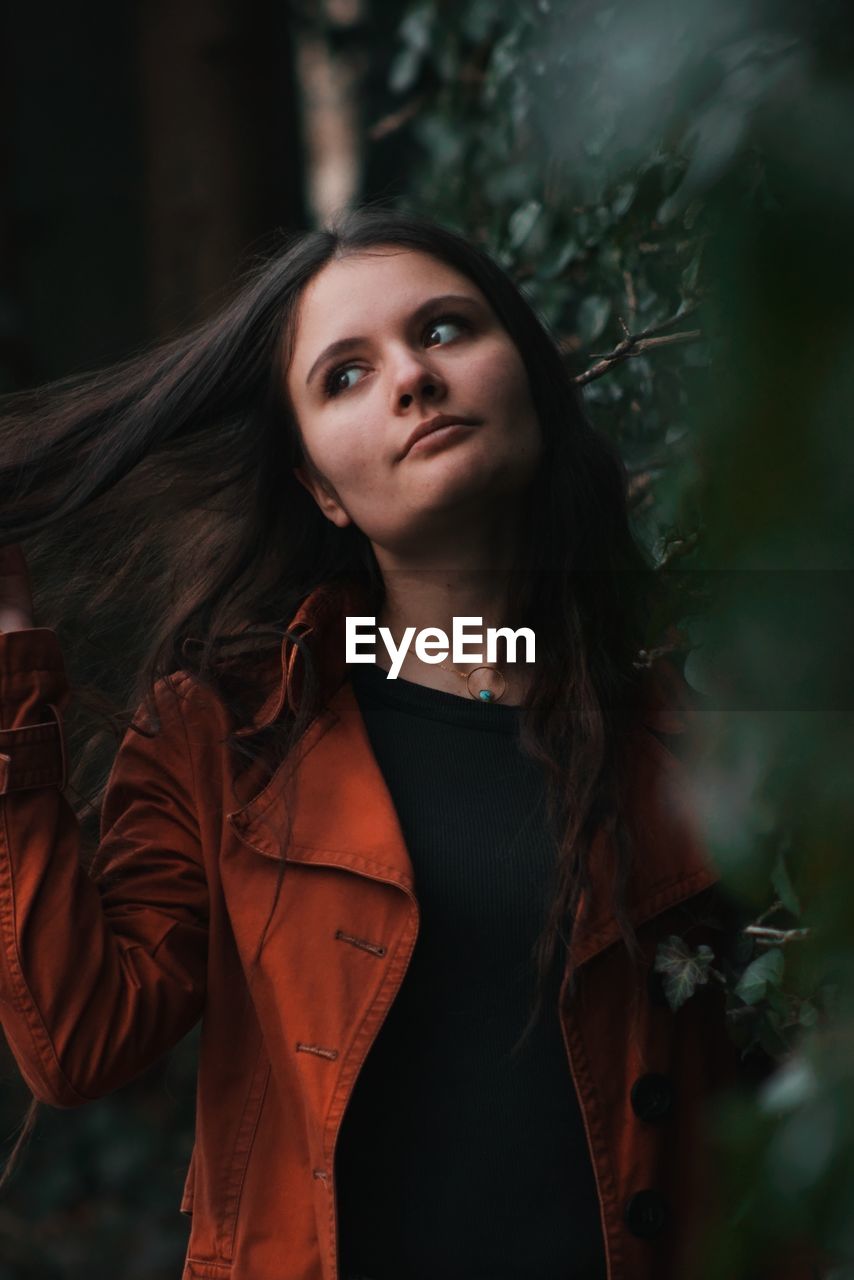 Beautiful young woman looking away while standing against plants