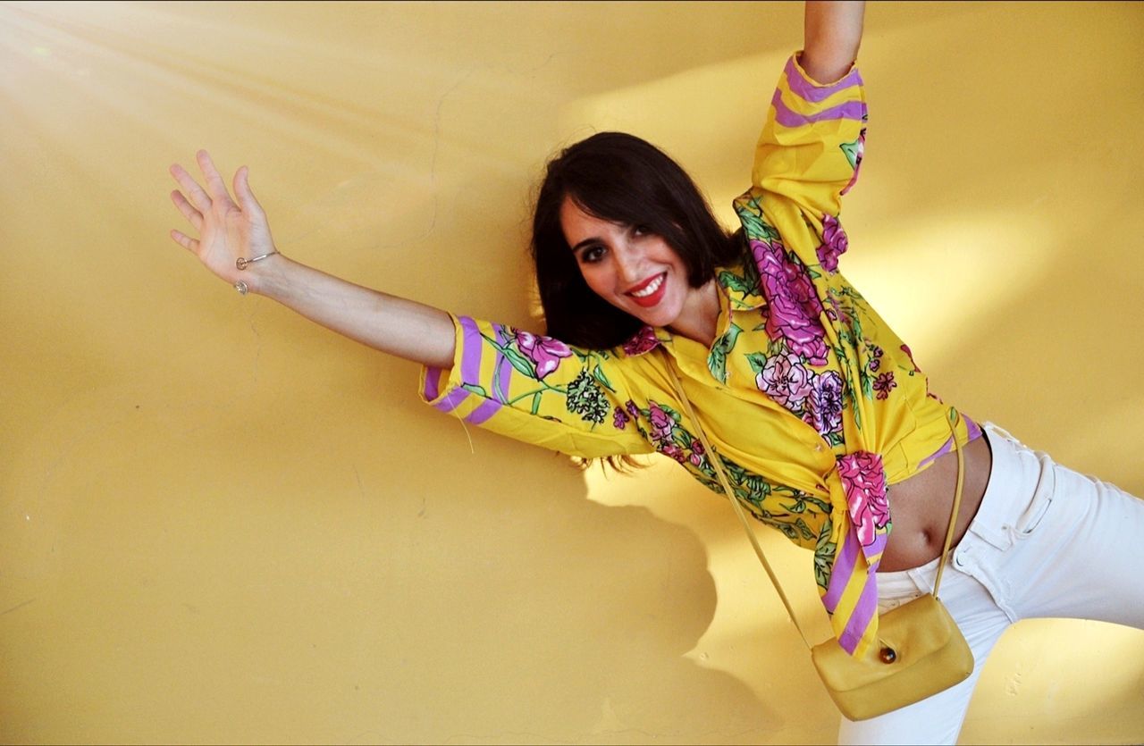 Portrait of smiling young woman against yellow wall