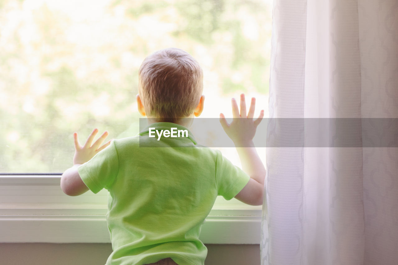 Rear view of boy standing by window at home