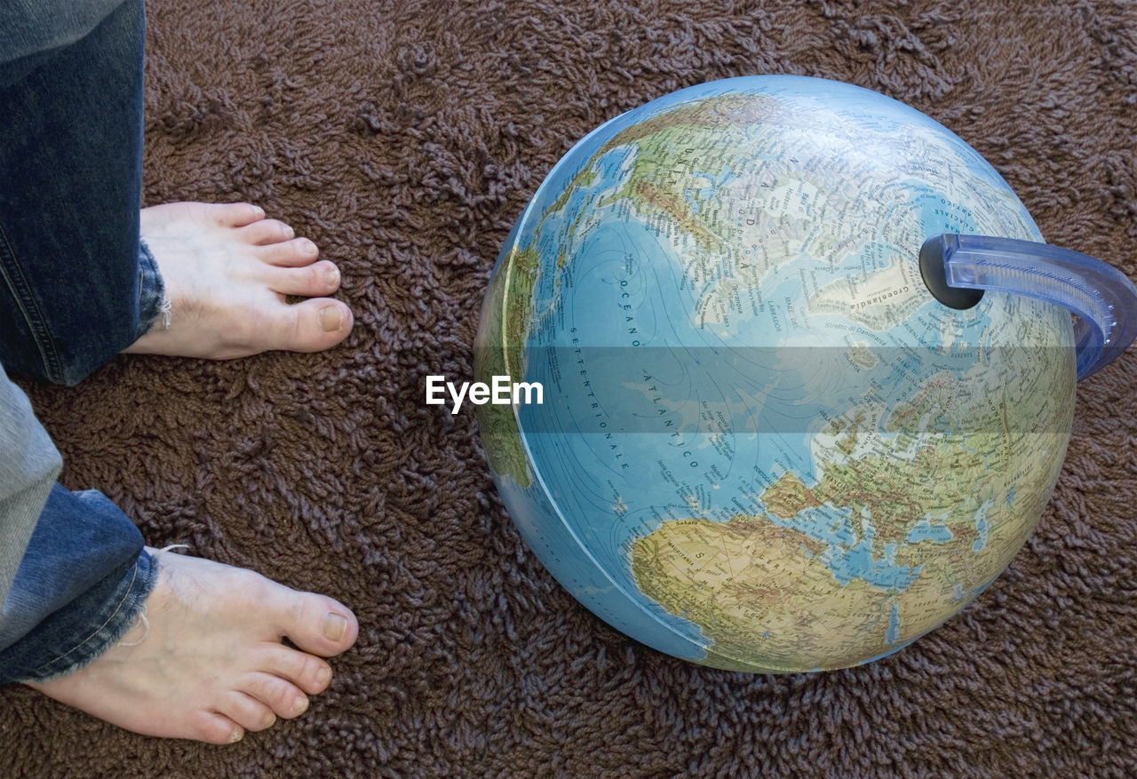 Low section of man standing by globe on rug at home