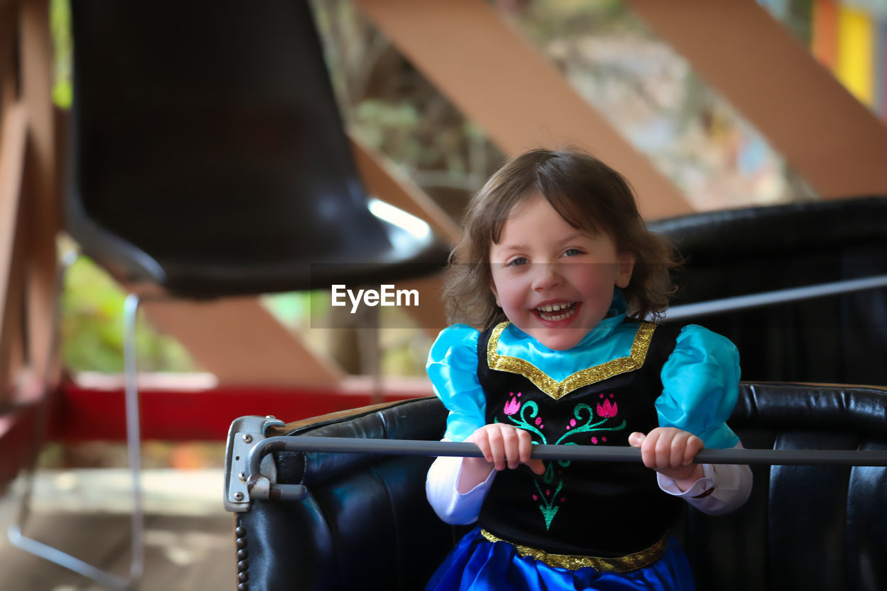 Portrait of smiling cute girl sitting in bumper car at amusement park