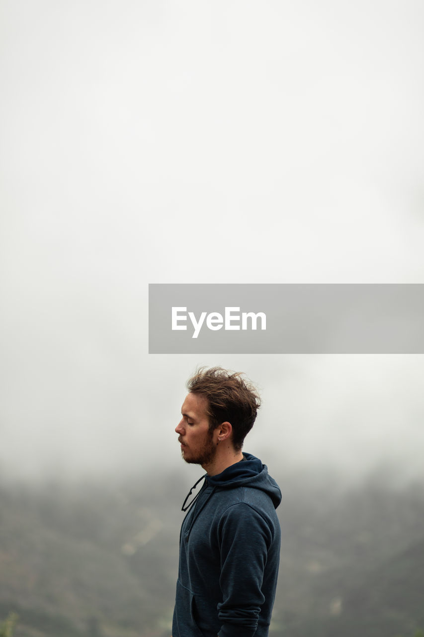 Side view thoughtful male hiker standing on mountain summit in highlands in seville on overcast misty weather