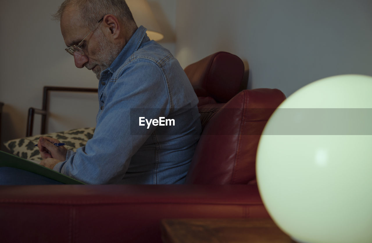 Portrait of adult man sitting on sofa at home and reading document files.