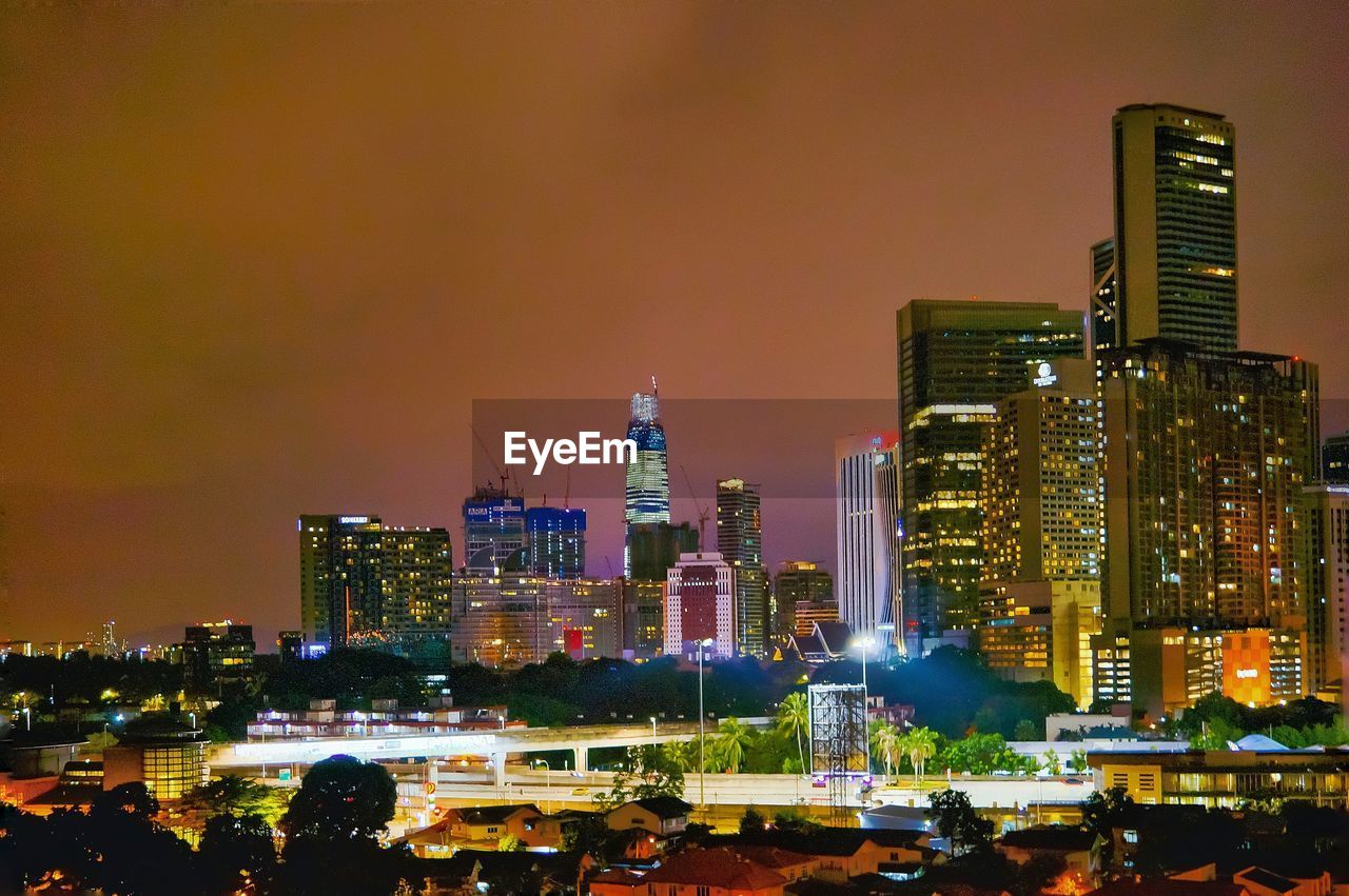 Illuminated modern buildings in city against sky at night