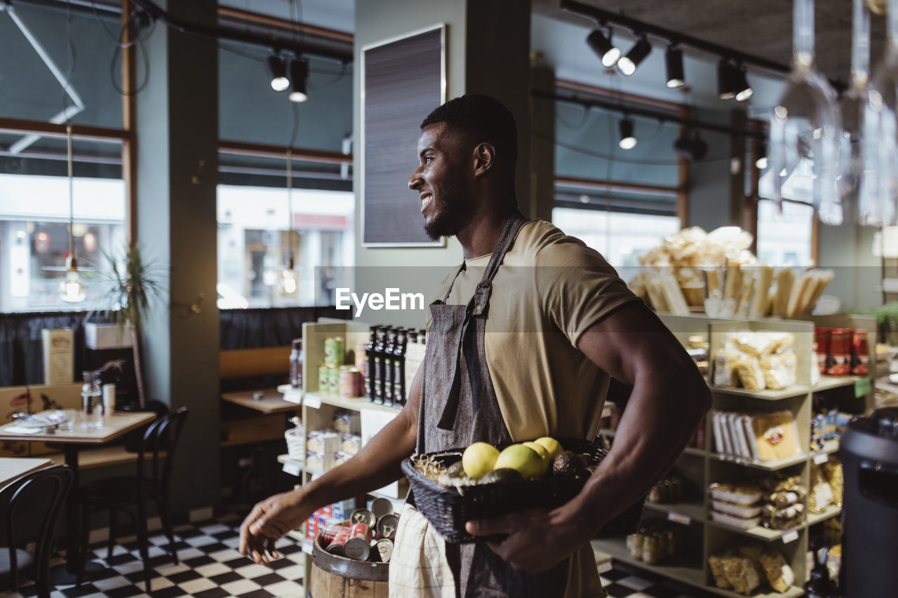 Young male owner standing with fruit basket in deli store