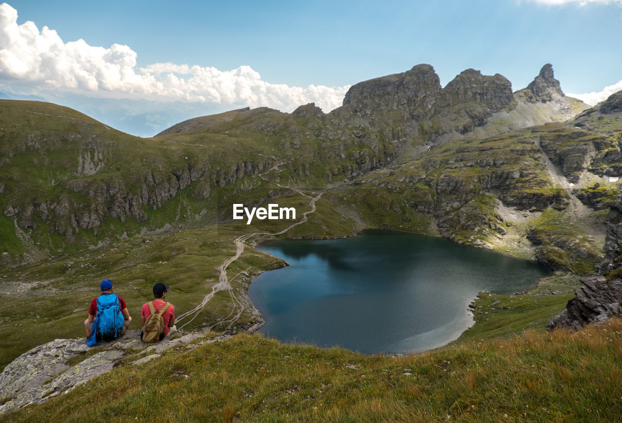 Rear view of hikers sitting by lake on mountain