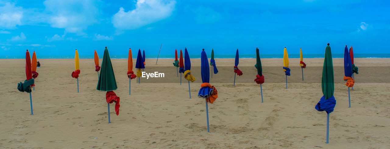 Panoramic view of closed parasols at beach against sky