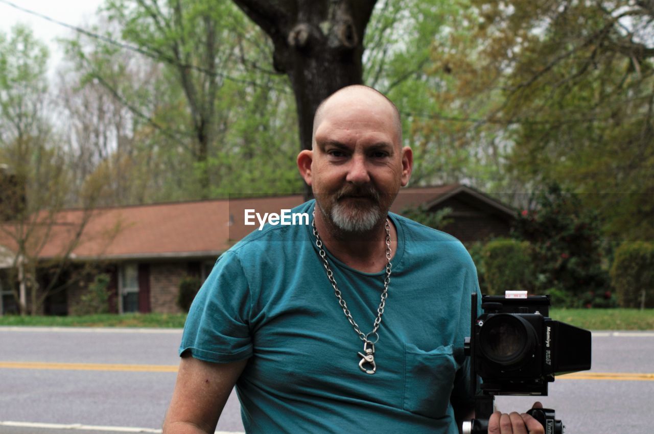 Portrait of bald mature man photographing against trees