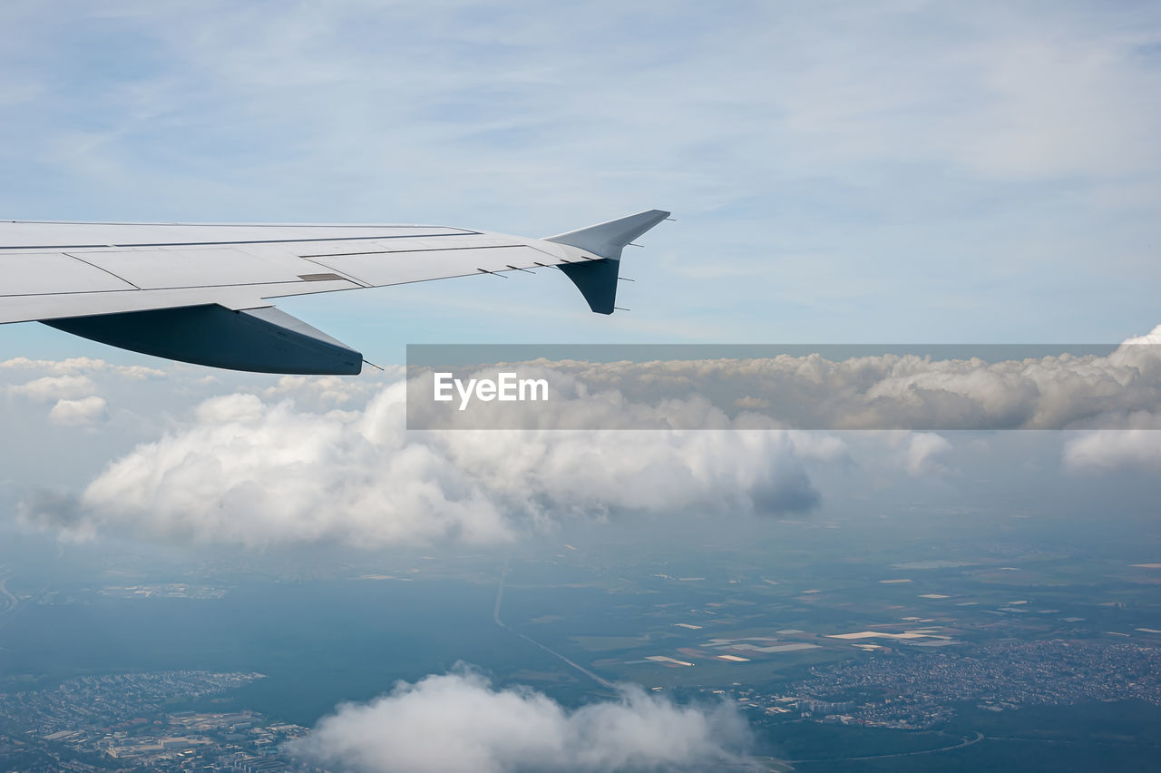 View from airborne airplane window at cloudy sky and land with fields from high altitude.