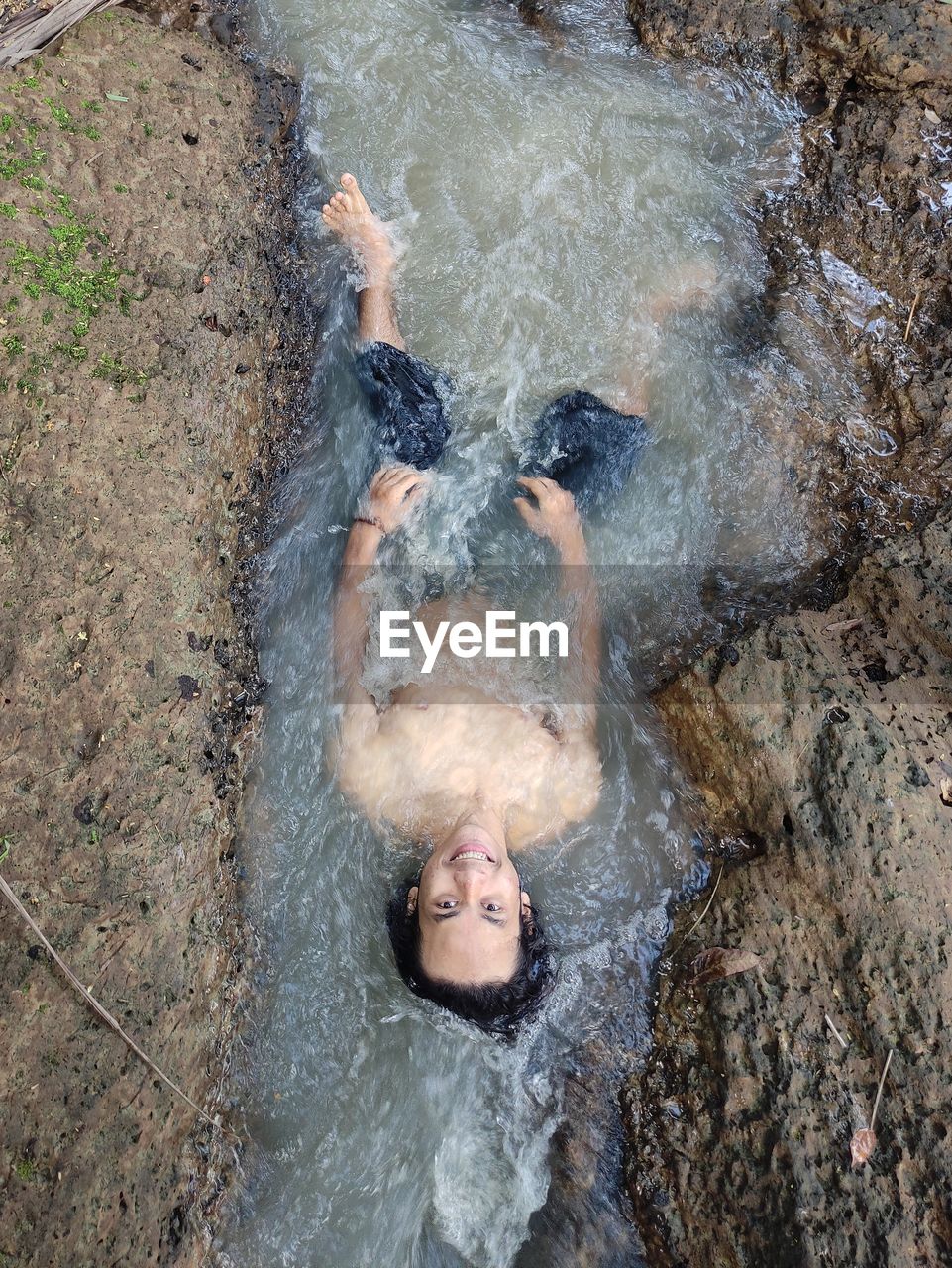High angle view of shirtless man lying in stream