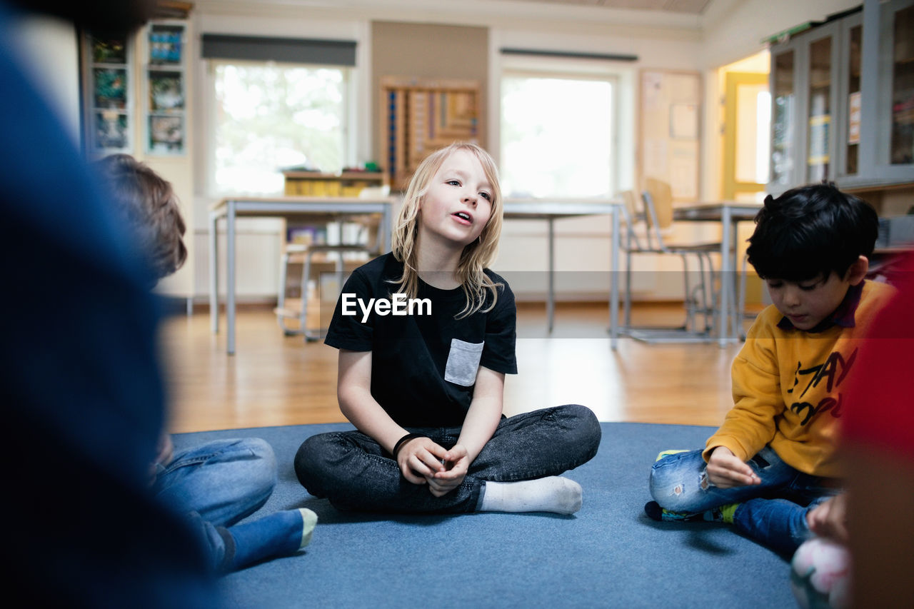 Girl talking while sitting with friends on floor in classroom