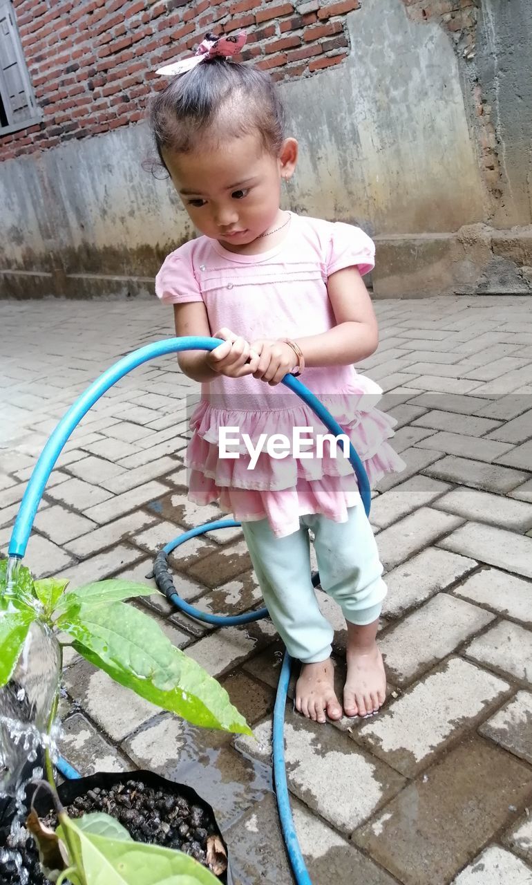 FULL LENGTH OF CUTE GIRL STANDING ON FOOTPATH BY A BICYCLE