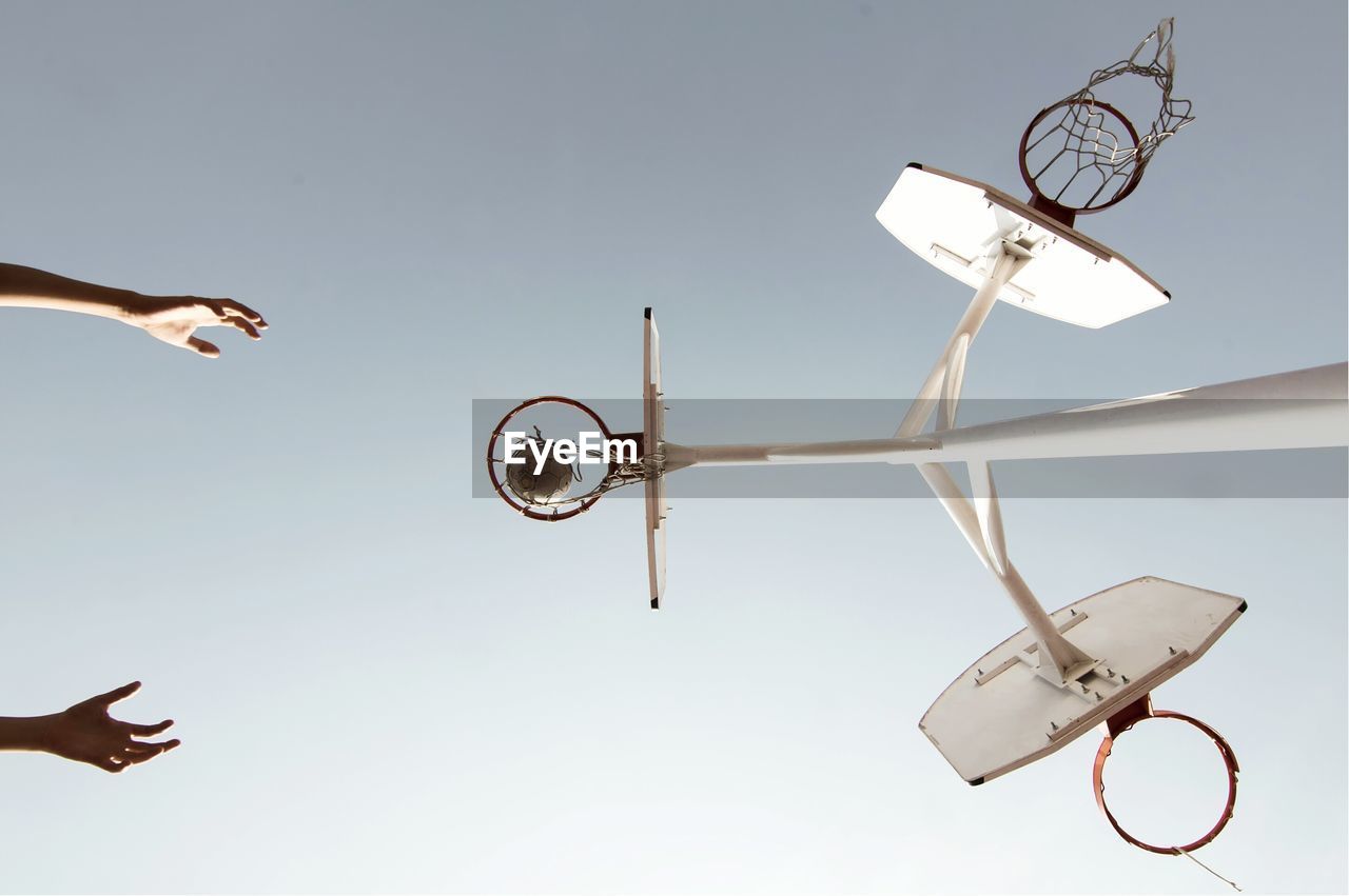 Cropped hands of man playing basketball against clear sky