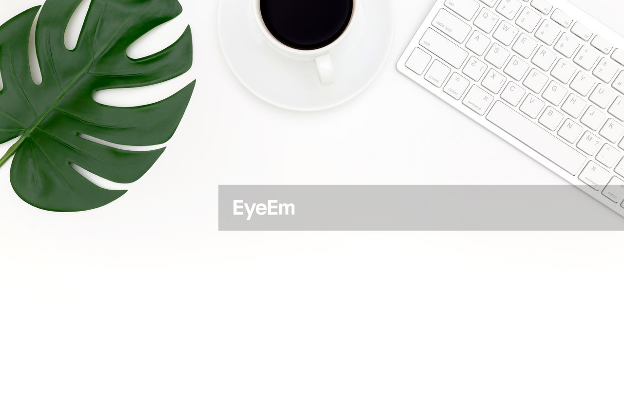 COFFEE CUP AND LAPTOP ON TABLE AGAINST WHITE BACKGROUND