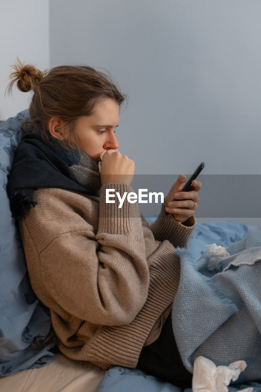 Young girl feeling sick, suffering from rhinitis or allergy. woman hold in hand phone. paper napkin