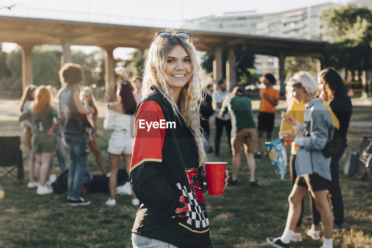Portrait of smiling woman with drink standing against friends at festival