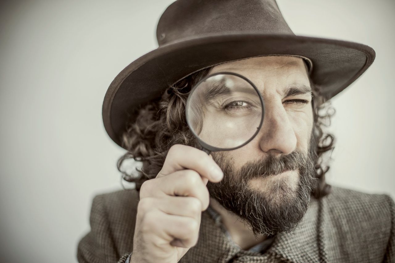 Close-up of hipster looking through magnifying glass against white background