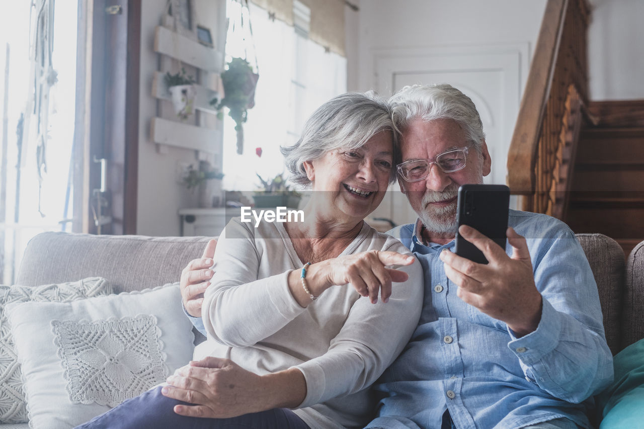 Senior couple looking at mobile phone while sitting on sofa at home