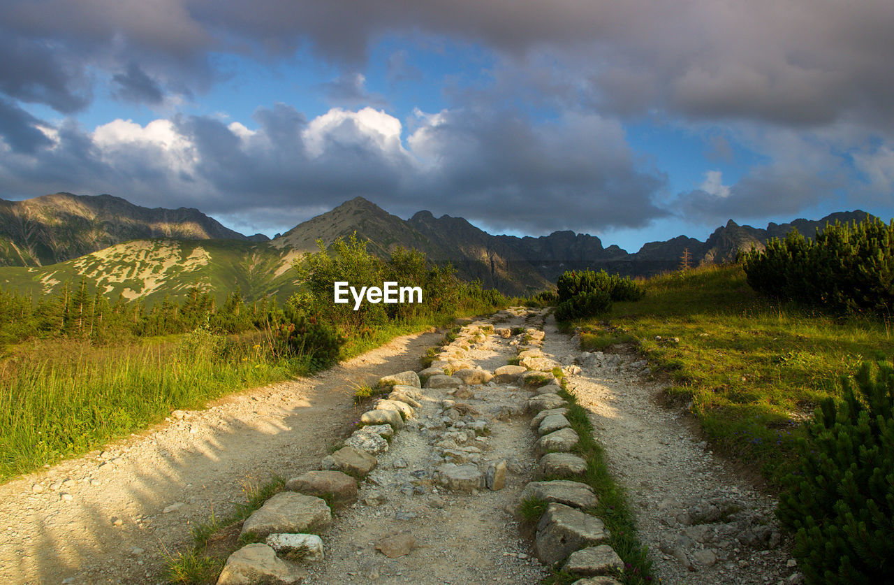 Dirt road leading towards mountains against sky