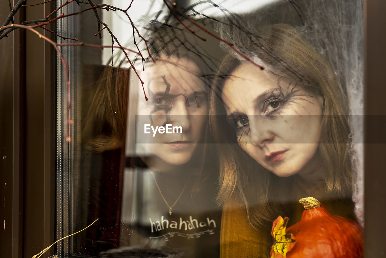 Two female witches look through a spider web ominously out of the window. halloween party.