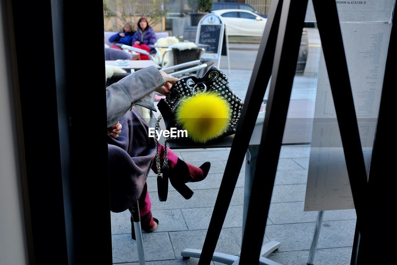 Low section of woman sitting at sidewalk cafe seen through window