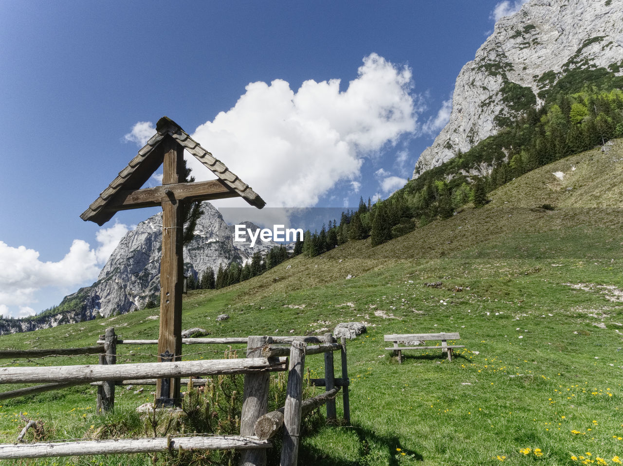 Cross on field against sky and mountains 