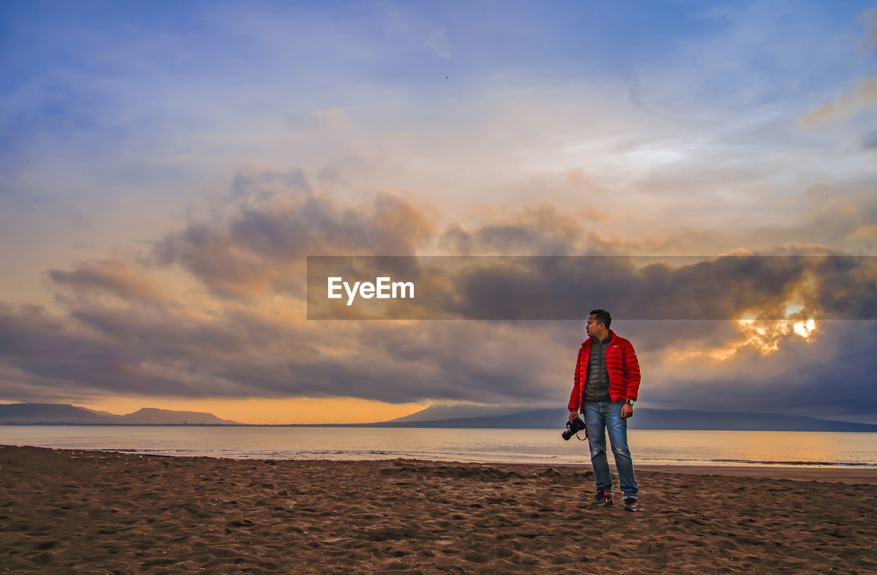 FULL LENGTH OF PERSON STANDING ON BEACH AGAINST SKY DURING SUNSET