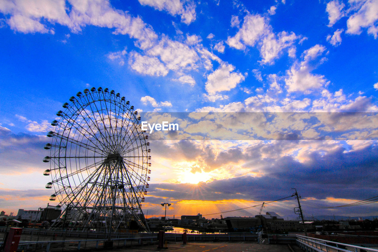 sky, ferris wheel, amusement park ride, amusement park, cloud, arts culture and entertainment, sunset, architecture, nature, travel destinations, built structure, city, sunlight, travel, blue, transportation, no people, carnival, outdoors, traveling carnival, dusk, evening, tourism, recreation, horizon, landscape
