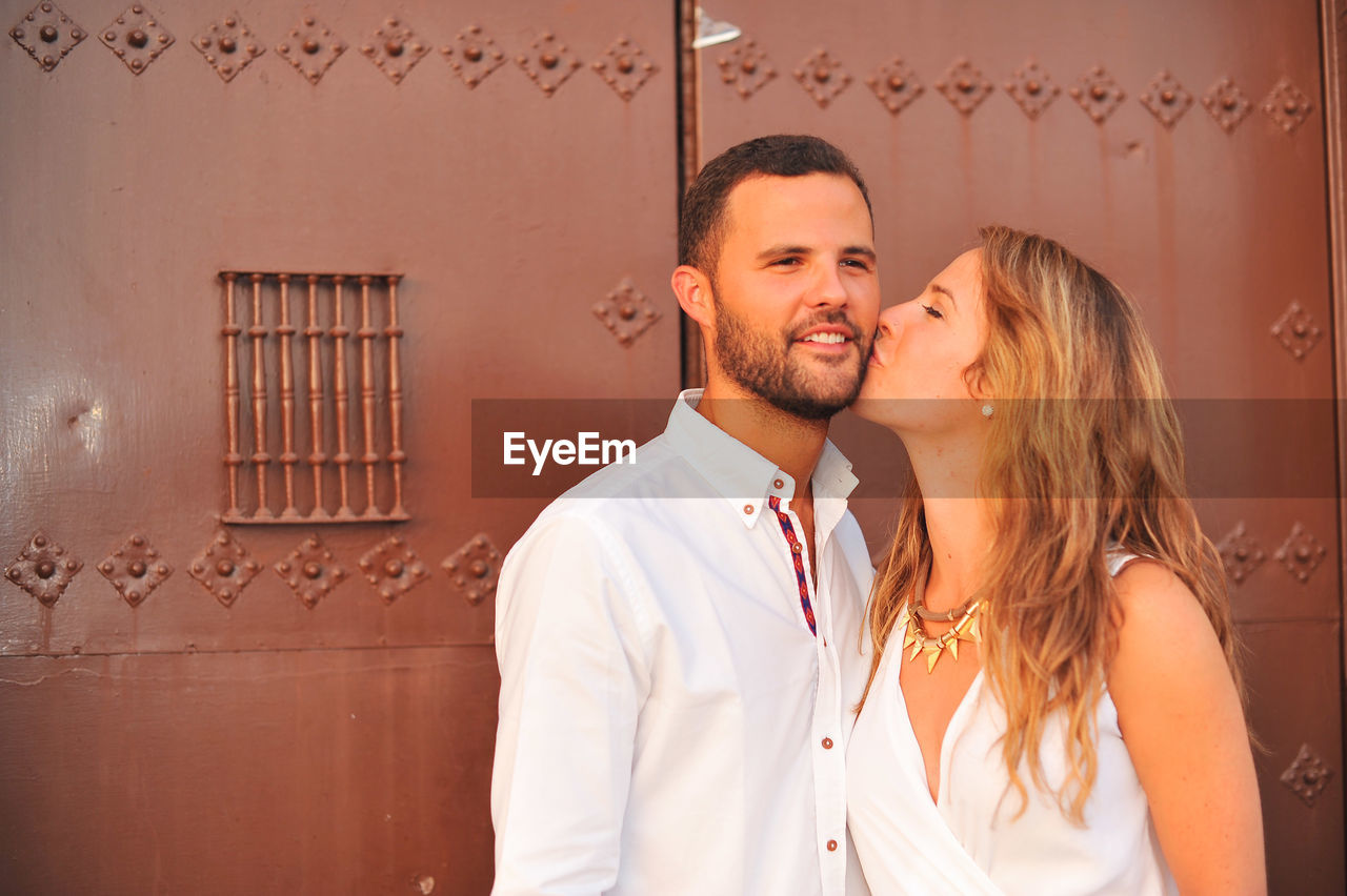 Young woman kissing man against closed door of historic building