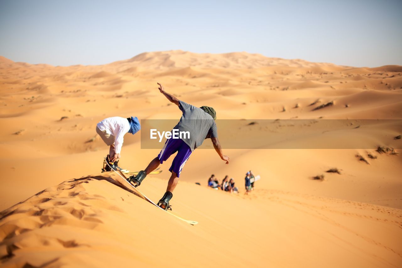 People sandboarding in desert against clear sky