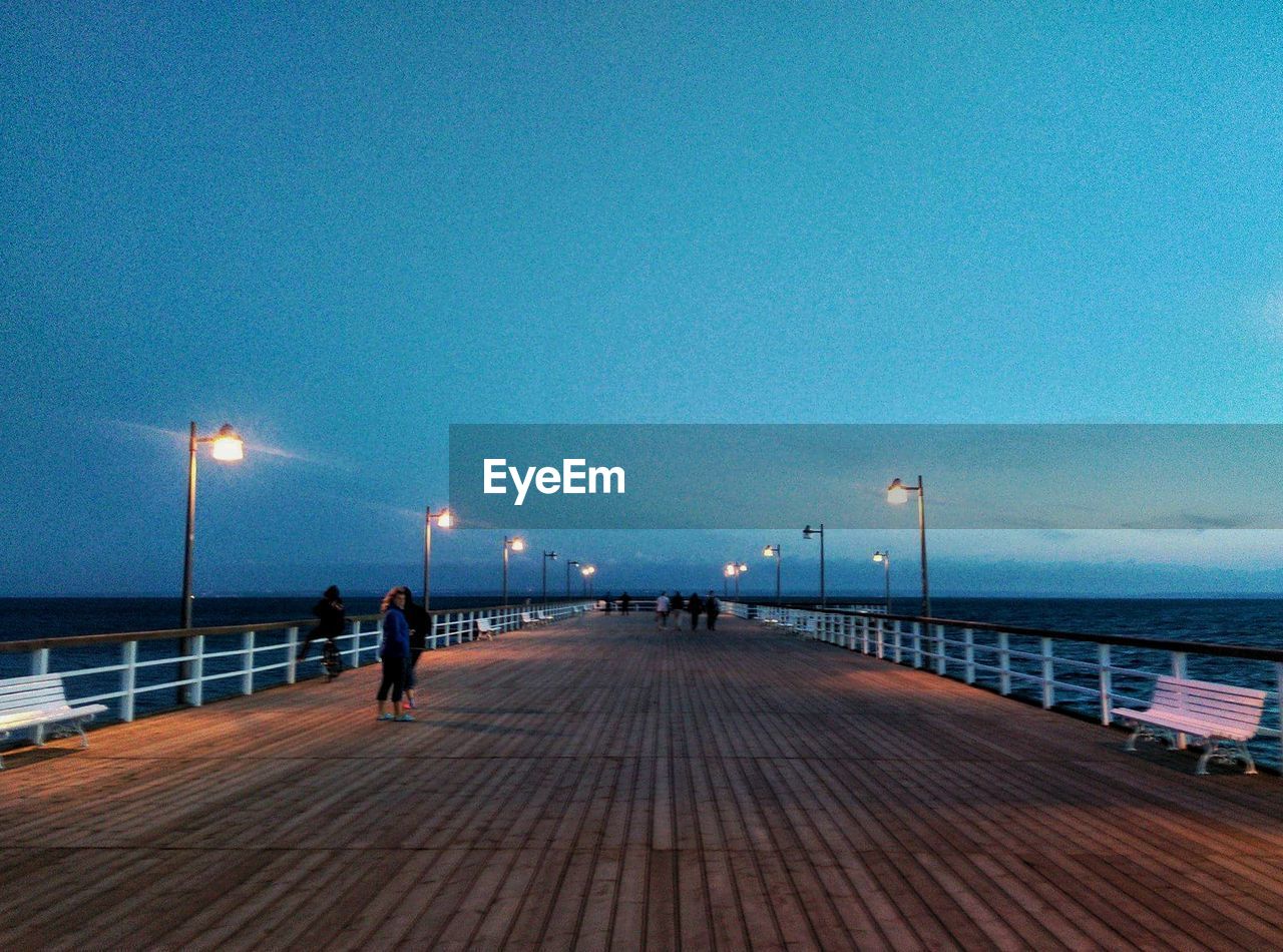 PEOPLE ON PIER AT HARBOR AGAINST CLEAR SKY AT NIGHT