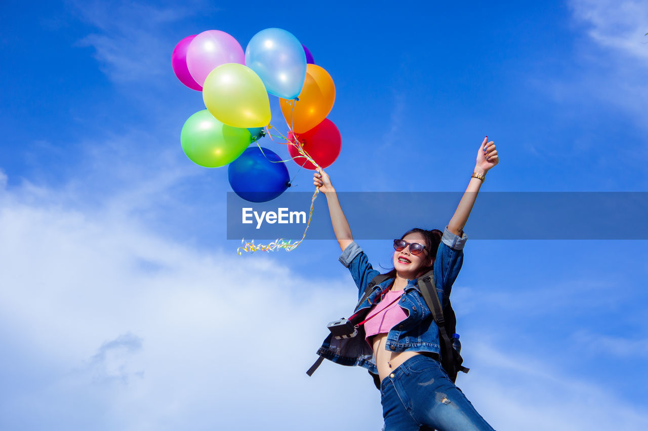 Woman with backpack holding colorful balloons against cloudy sky