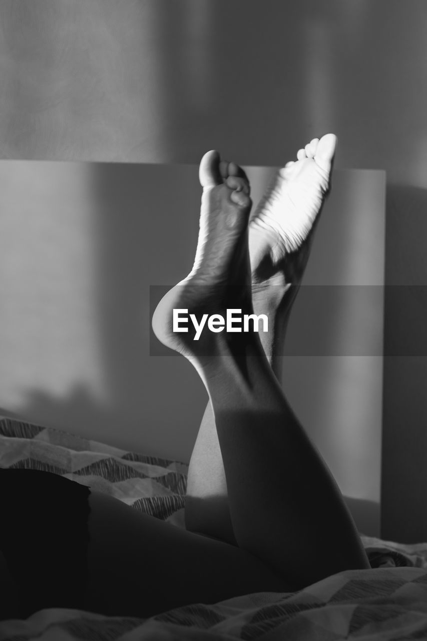Close up barefoot legs lying on bed monochrome concept photo