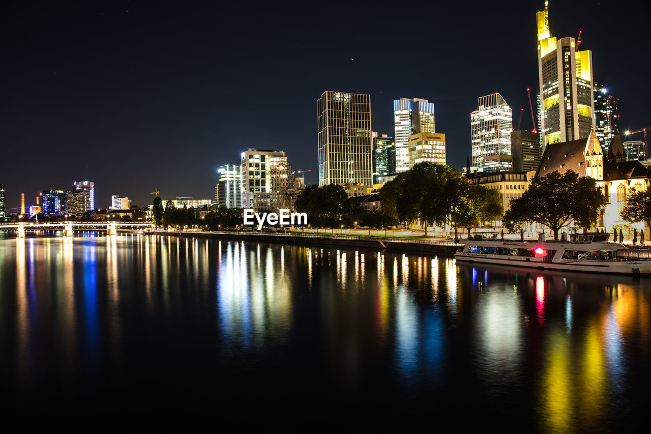 River by illuminated buildings against sky at night